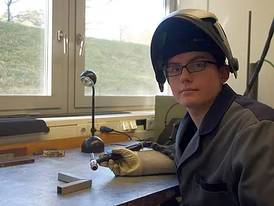 Daniel Sailer bearbeitet ein Werkstück in der Schweißwerkstatt. Schutzkleidung und Schweißschutzhelm sind Pflicht, damit Haut und Augen keinen Schaden nehmen. 