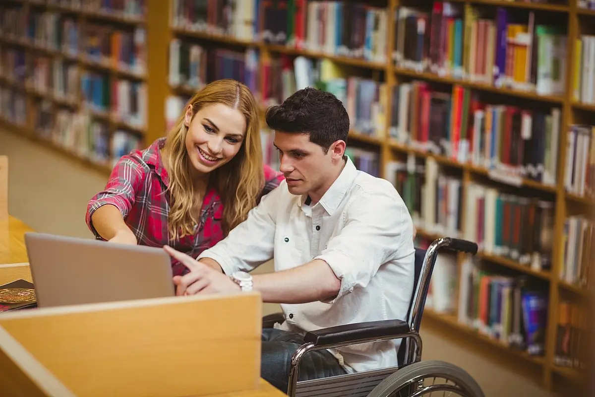 Student im Rollstuhl arbeitet in einer Bibliothek mit einer Studentin
