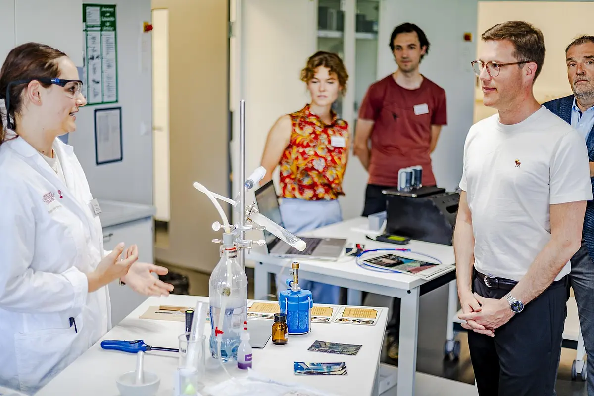 Frau in Laborkittel an Tisch mit Experimentierbedarf im Gespräch mit Manuel Hagel