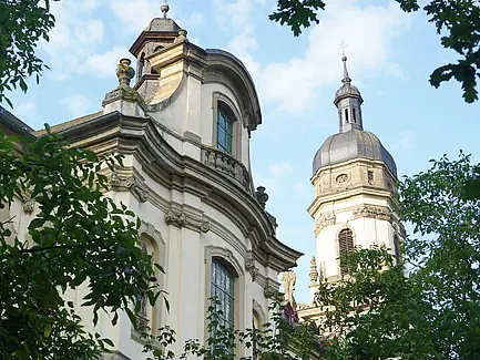 Das Bild ist gerahmt von einem grünen Blätterdach. In der Mitte ist die Fassade des Klosters und ein Turm des Klosters in Schöntal zu sehen.
