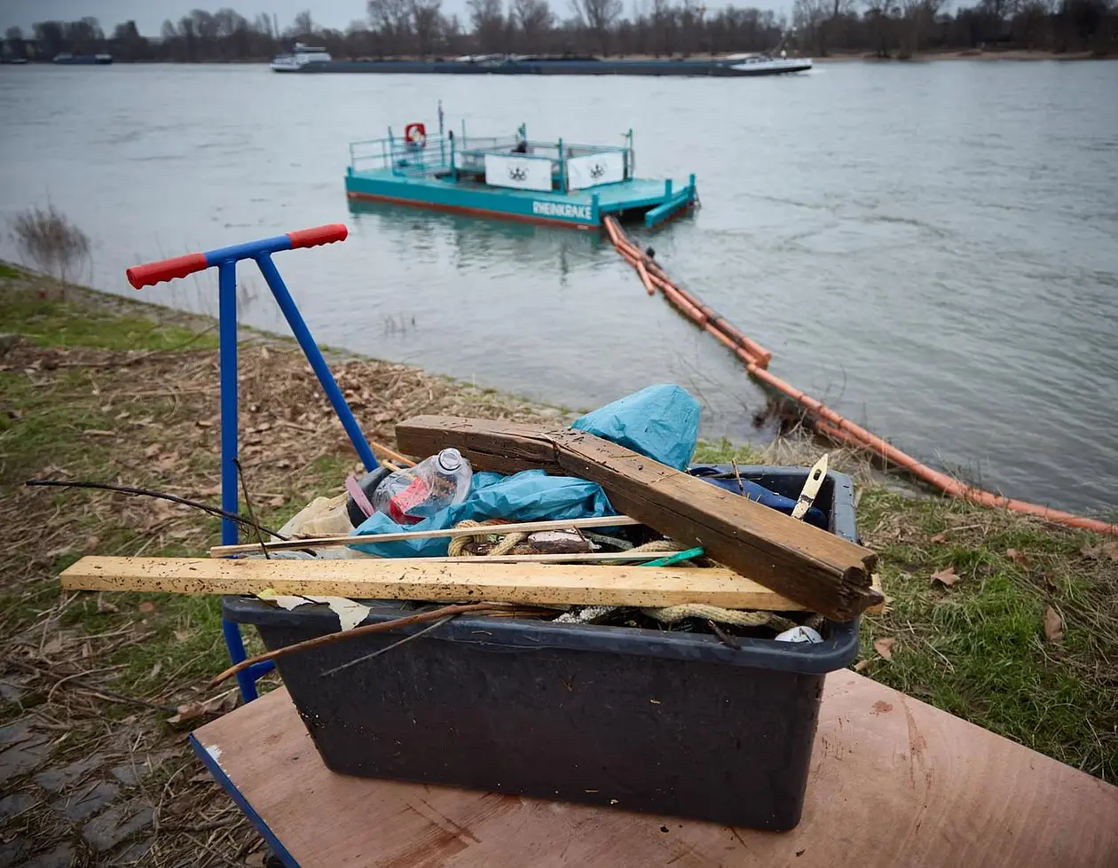Kiste mit Müll, im Hintergrund der Rhein mit der schwimmenden Müllfalle