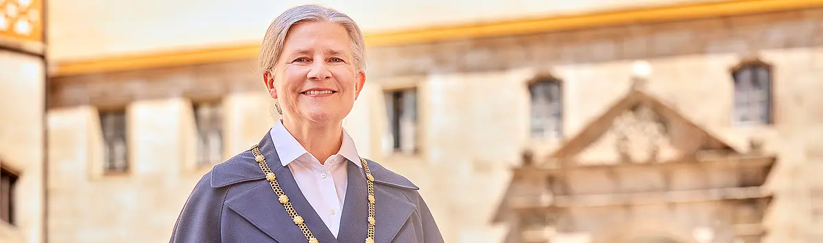 Portrait der Rektorin der Universität Tübingen, im Hintergrund ist ein Teikl des Schlosses Tübingen zu sehen. 
