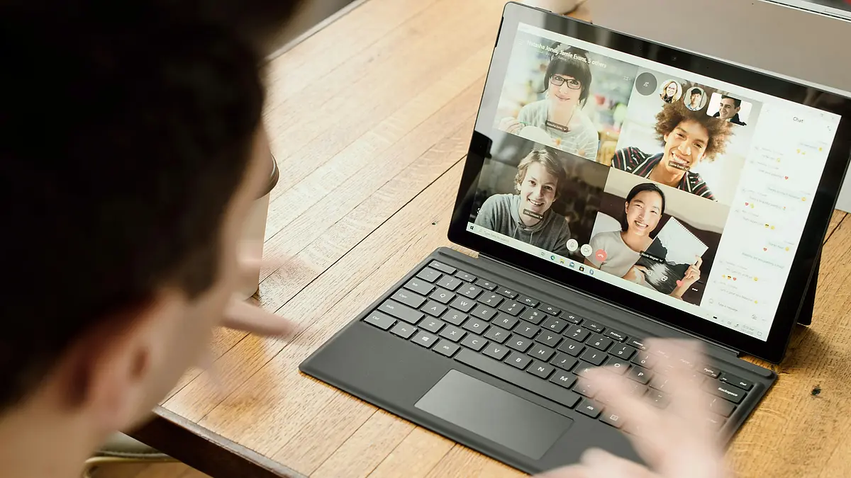 Person sitzt vor seinem Laptop, Video-Konferenzteilehmerinnen sind zu sehen