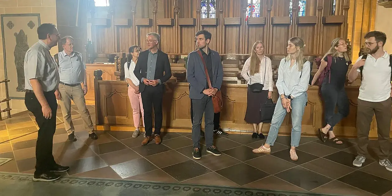 Auf dem Bild sind insgesamt zehn Menschen zu sehen, die teilweise an einer Kirchenbank lehnen. Bei den zehn Menschen handelt es sich um Teilnehmende des Oberseminars - dazu zählen z.B. Prof. Kranemann und Prof. Wahle, 
