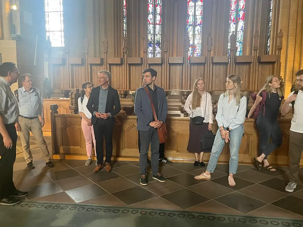 Auf dem Bild sind insgesamt zehn Menschen zu sehen, die teilweise an einer Kirchenbank lehnen. Bei den zehn Menschen handelt es sich um Teilnehmende des Oberseminars - dazu zählen z.B. Prof. Kranemann und Prof. Wahle, 