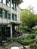 Links ist die Bibliothek des Theologicums abgebildet. Studierende sitzen im Freien um die Tische der Cafeteria. 