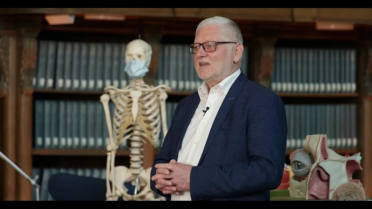 Der Tübinger Virologe und Biologe Professor Thomas Iftner bei seinem Vortrag im historischen Lesesaal. Hinter ihm steht ein Skelett mit medizinischem Mundschutz.