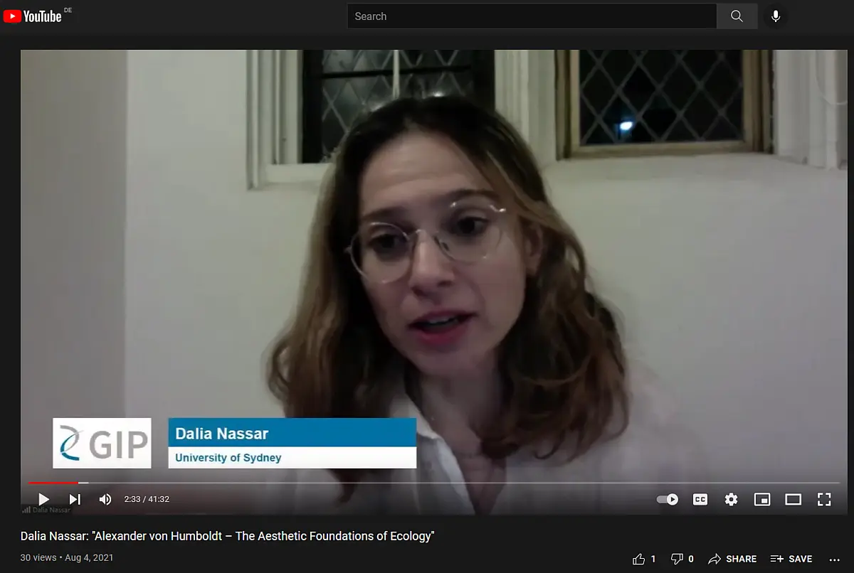 A woman in her early 30s with shoulder length hair speaks into a webcam