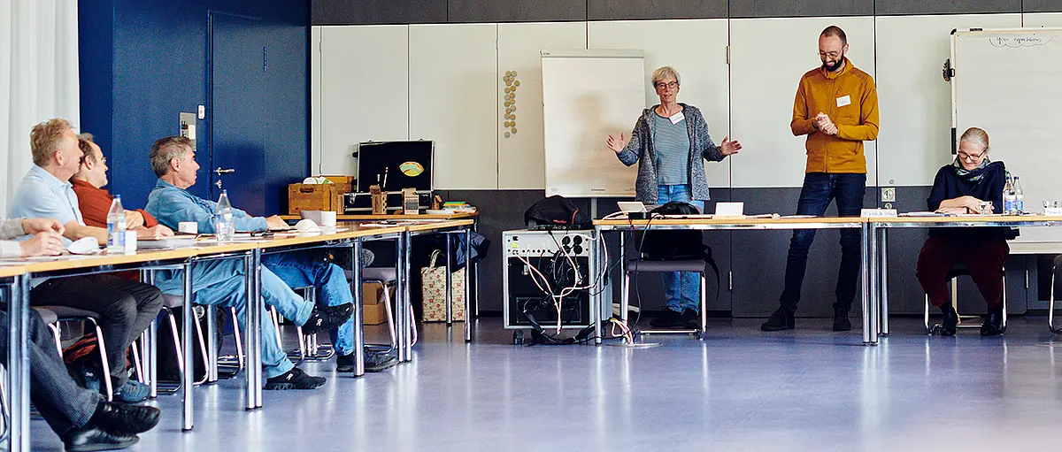 Sechs personen, die bei einer Cluster-Konferenz gemeinsam im Hörsaal sitzen und diskutieren