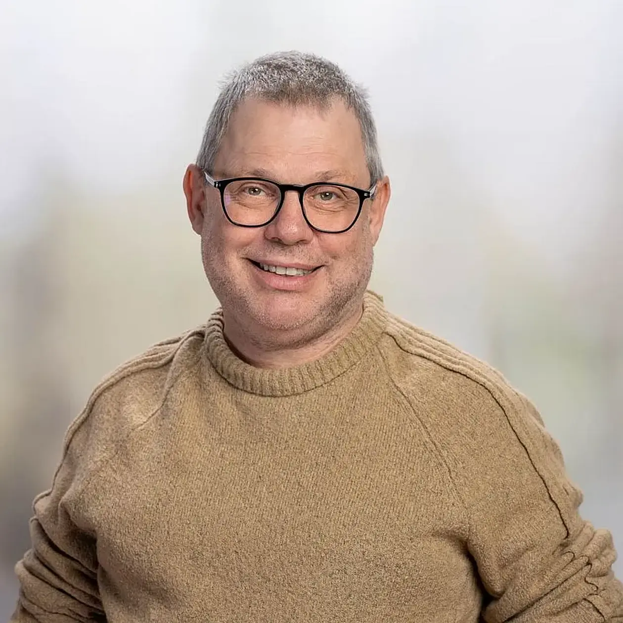 A portrait photo of Gerhard Jäger, a white middle aged man with a buzzcut and glasses with black frames facing the camera smiling. He wears a beige turtleneck sweater. 