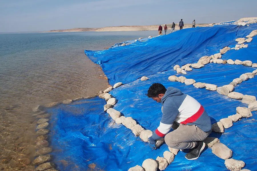 Ein Arbeiter befestigt Steine auf einer blauen Plastikfolie, um die Fundstätte vor dem ansteigenden Wasser des Mosul-Stausees zu schützen