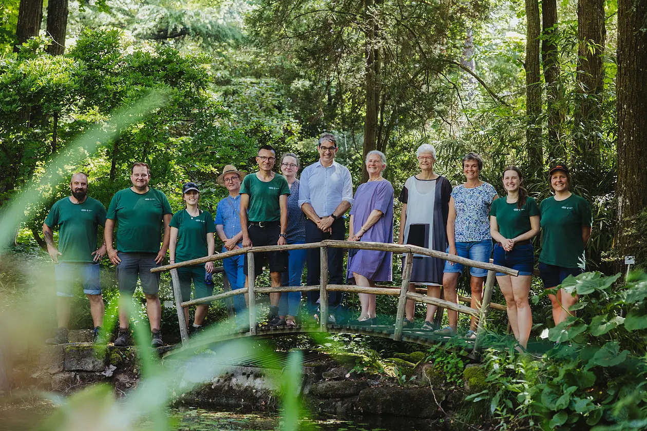 Menschen stehen auf einer Holzbrücke im Botanischen Garten, hinter ihnen sind Bäume.