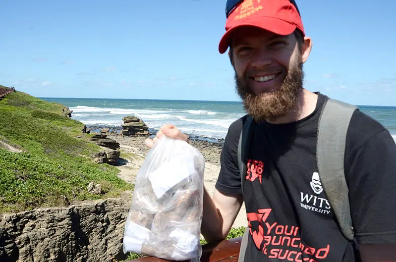 Das Foto zeigt Peter Morrissey mit Gesteinsproben an der Fundstätte der „Klasies-River-Höhlen“ in Südafrika 2021