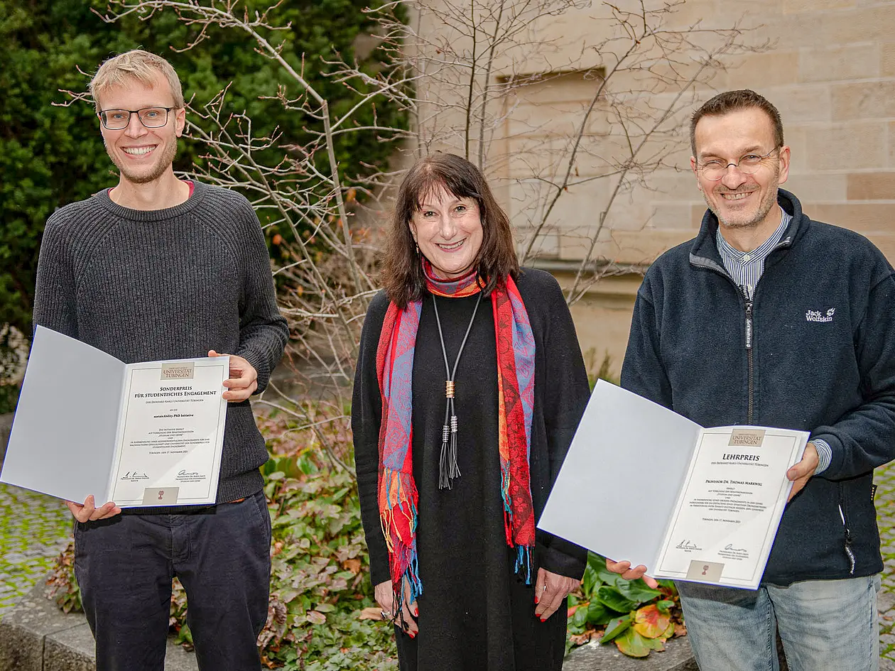 Cornelius Schröder und Thomas Markwig stehen rechts und links von Karin Amos, beide präsentieren eine Urkunde