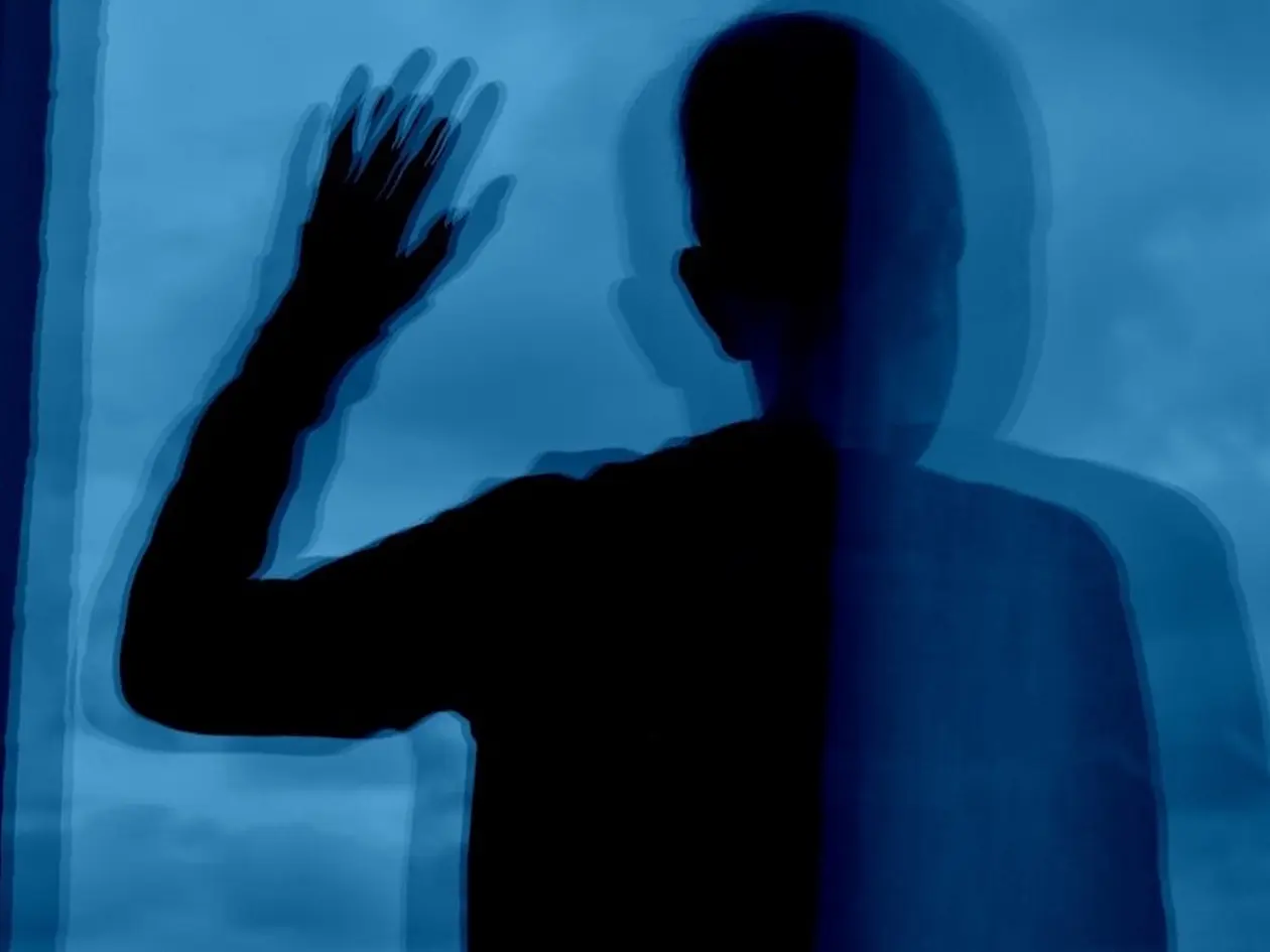 Eine Person spiegelt sich mehrfach in einer Fensterscheibe. Die bizarre Überlagerung der Spiege-lungen soll das veränderte Handlungsempfinden von Patientinnen und Patienten mit Schizophrenie darstellen.