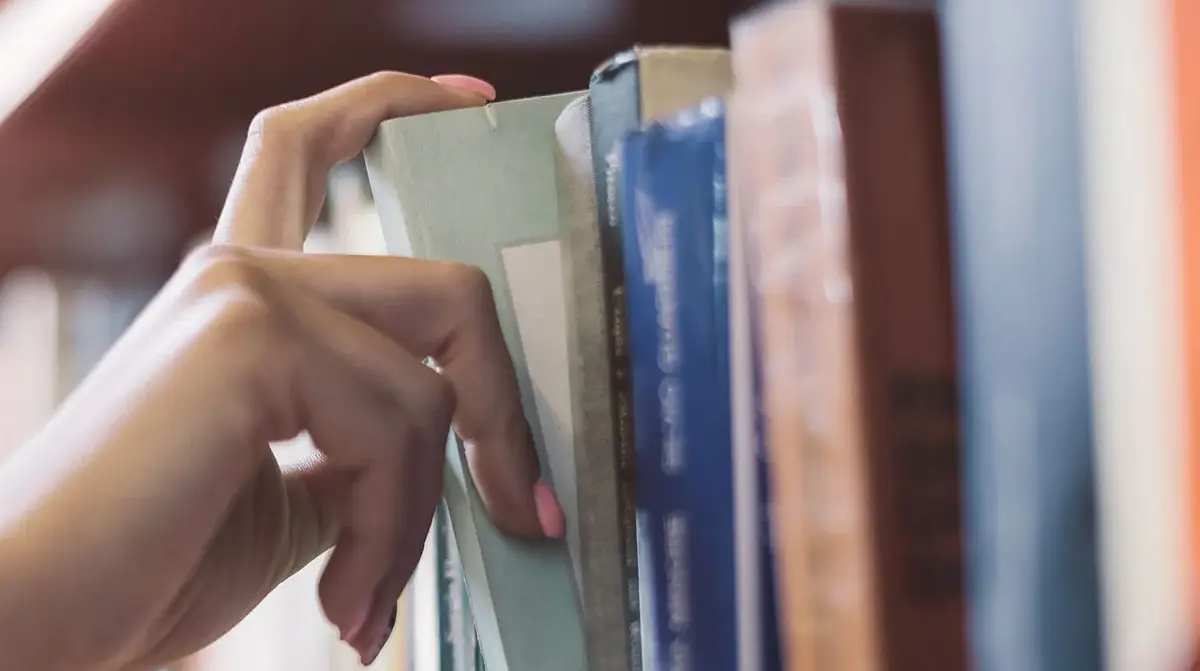 Hand removing a book from bookshelf.