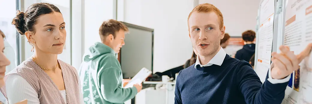 Menschen in einem Büro, ein Mann zeigt auf eine Flipchart und erklärt etwas.