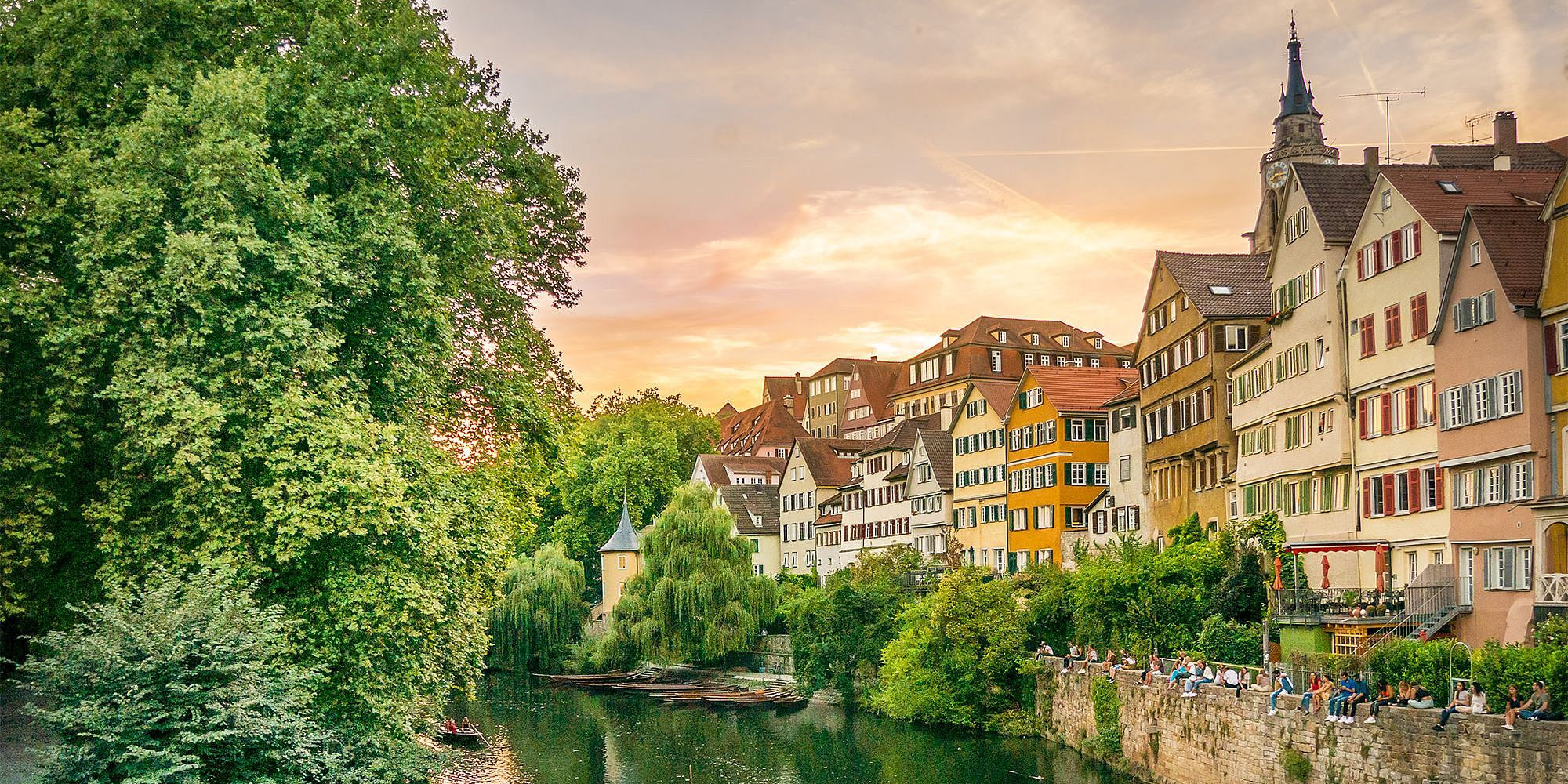View of the Tübingen Neckarfront with colorful historic houses lining the riverbank of the Neckar River, with the sunset in the background.