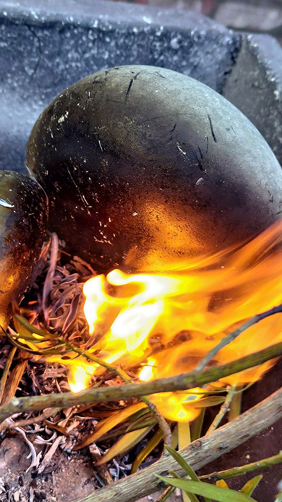 Visible is the resulting lump of tar, which is still in the fire next to flat smooth stones.