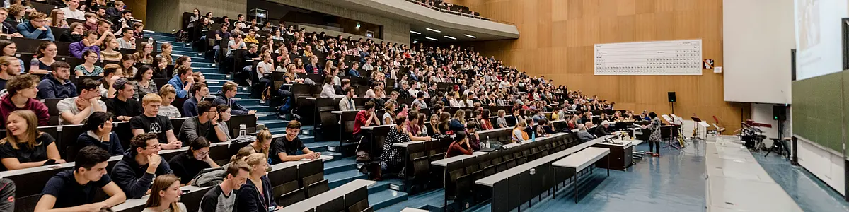 Viele Zuhörer sitzen in einem Hörsaal und eine Rednerin spricht am Pult.