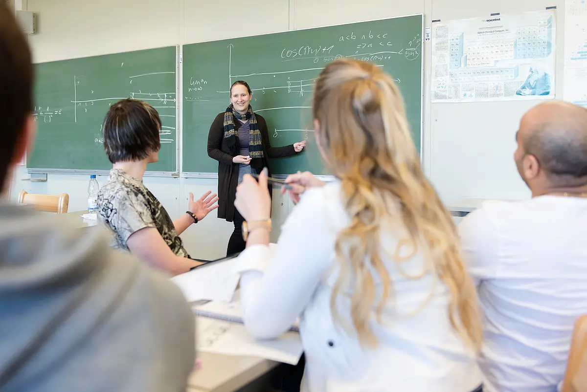 Dozentin erklärt den Studierenden etwas an der Tafel
