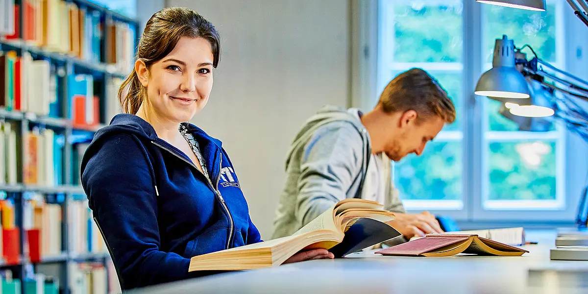 Zwei Studierende sitzen in der Bibliothek und lesen