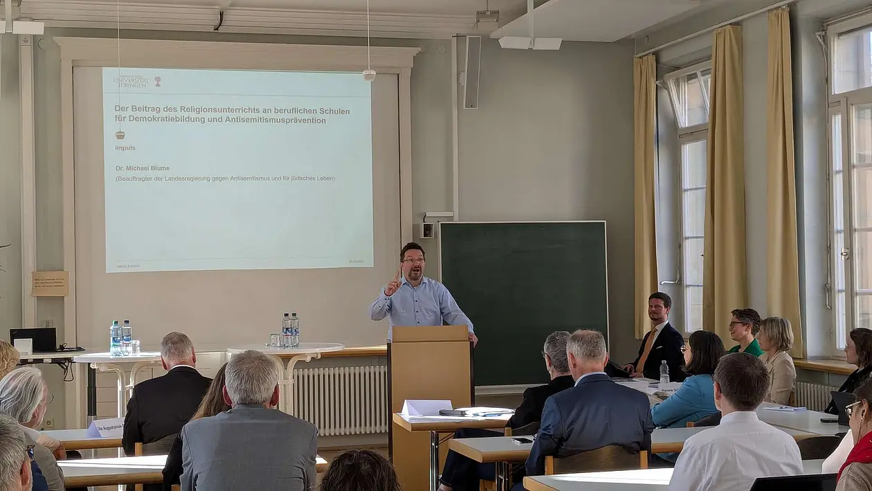 Eine Person hält einen PowerPoint-gestützten Vortrag in einem Seminarraum.