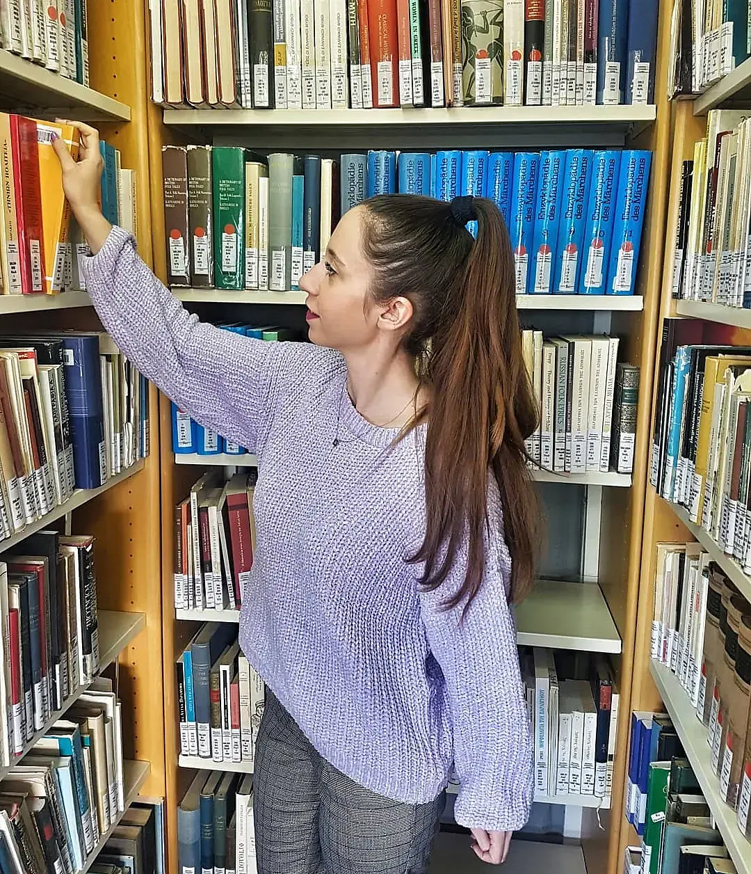 Katerina Schoina nimmt in einer Bibliothek ein Buch aus dem Regal