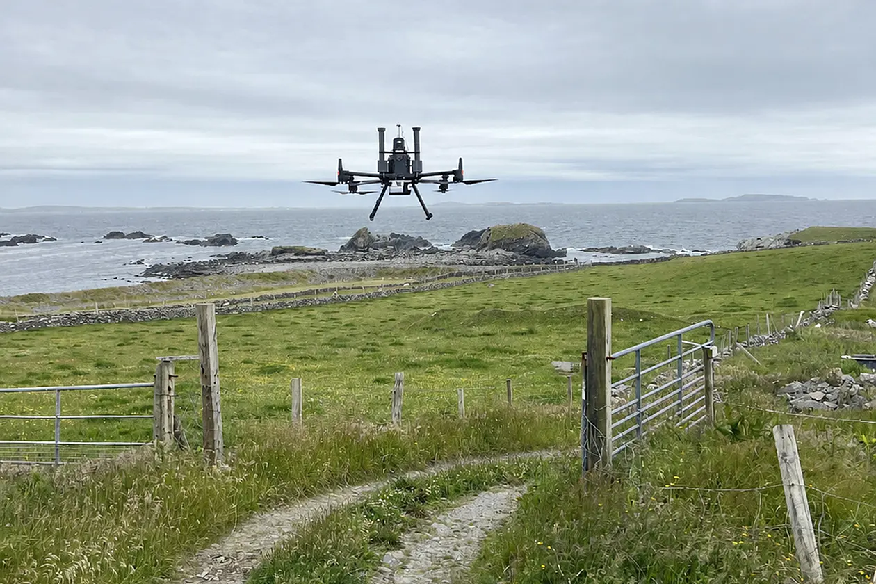Drone über Wiese, im Hintergrund Meer
