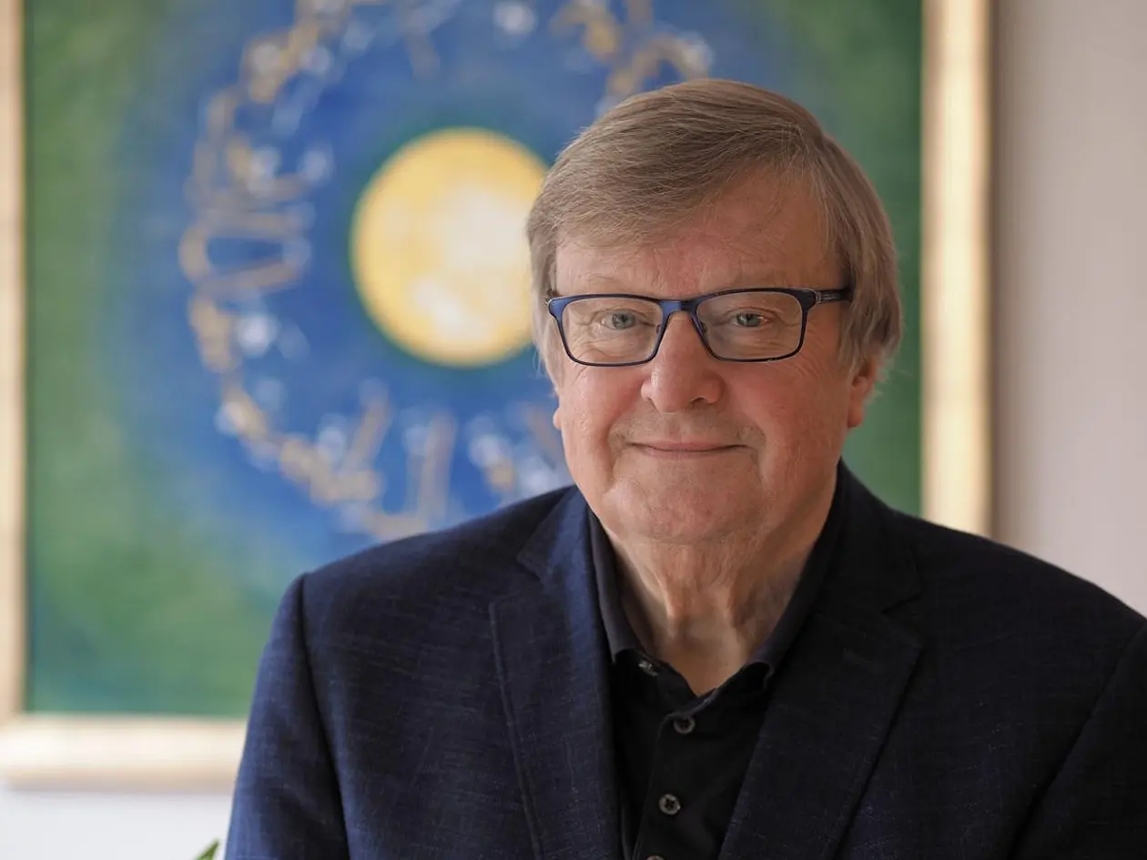 Porträtfoto von Professor Dr. Karl-Josef Kuschel vor einem grün-blau-gelb gemalten Bild