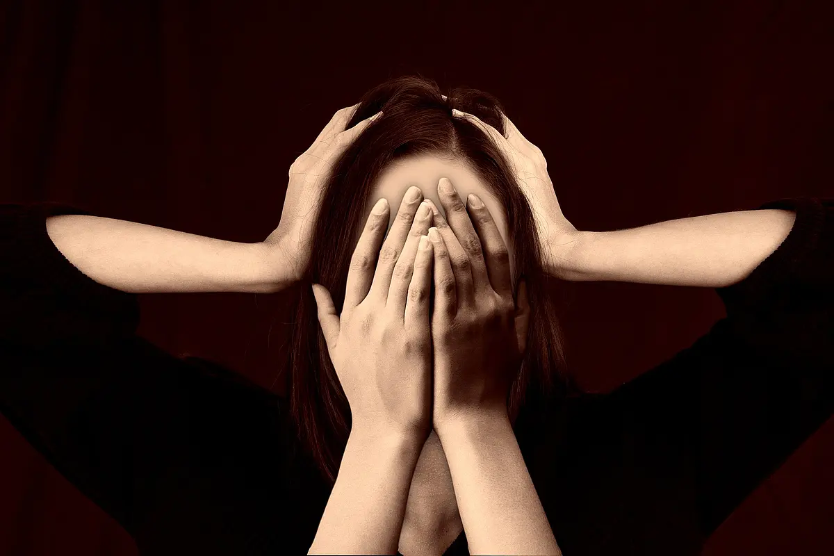 A woman holds her hands in front of her face and from the left and the right hands are pressing against her head.