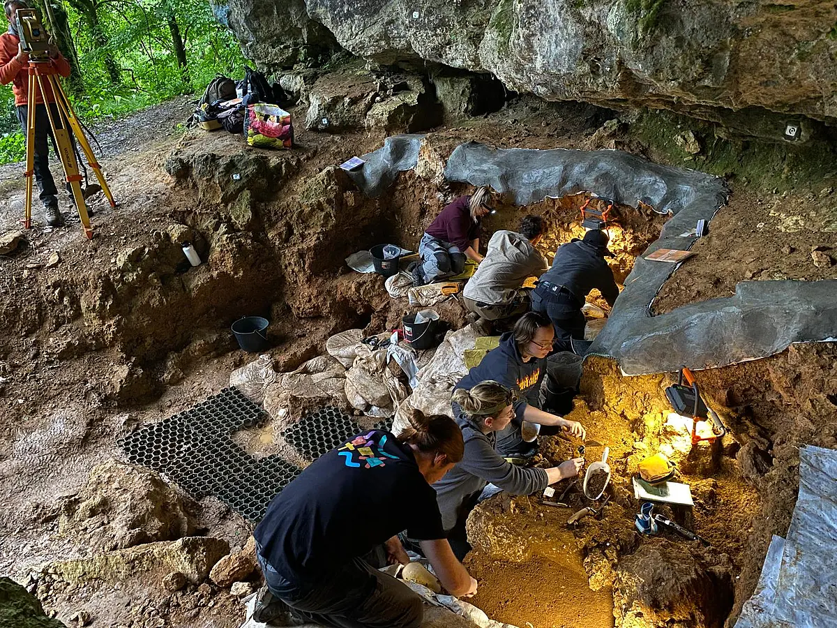 Sechs Personen knien auf dem Boden bei Ausgrabungen in der Höhle.