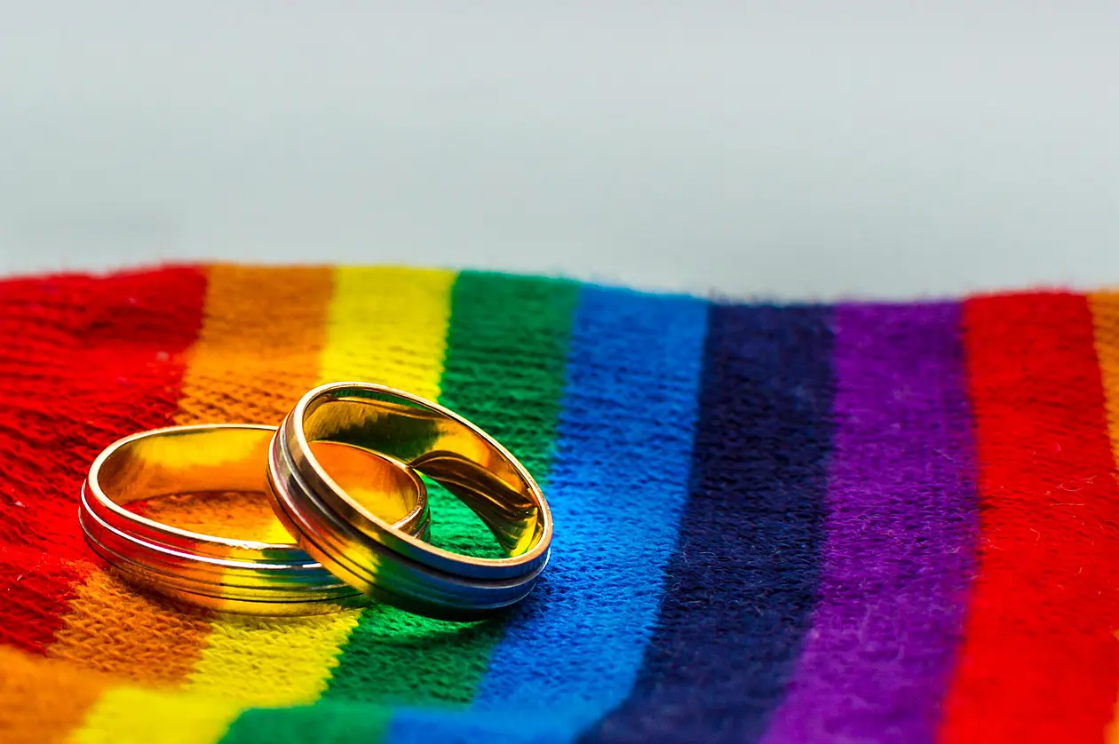 Eheringe liegen auf Stoff in Regenbogenfarben