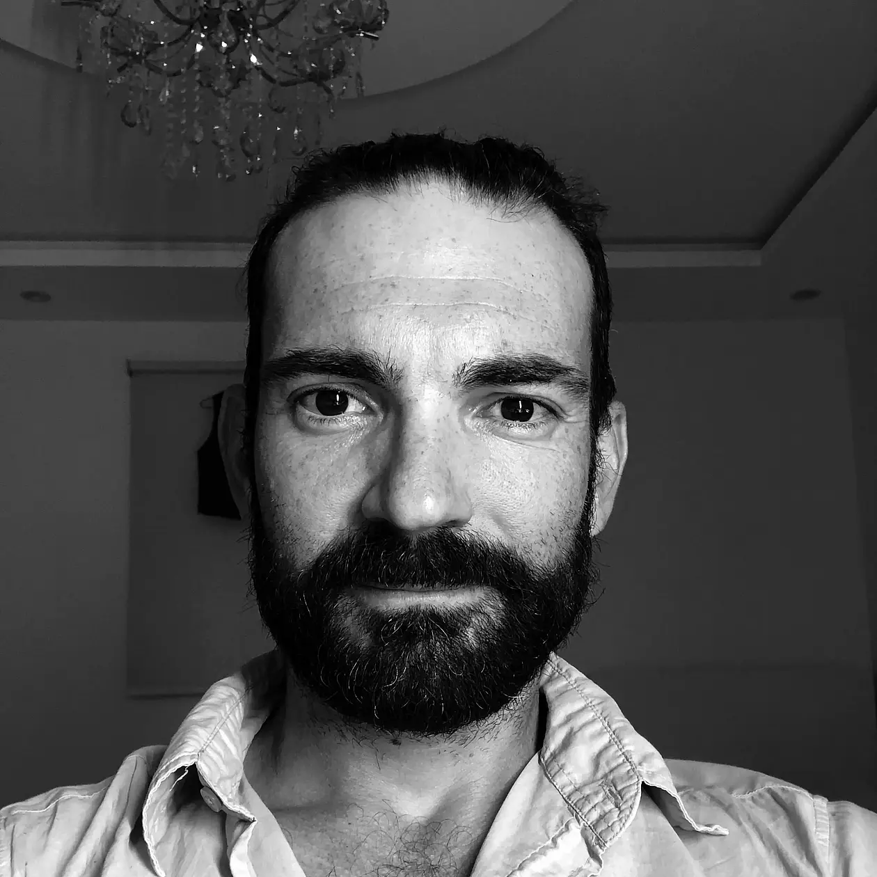 A black and white selfie shot of Yamandu Hilbert, a white man with a dark beard and dark hair, wearing a light button down shirt. 