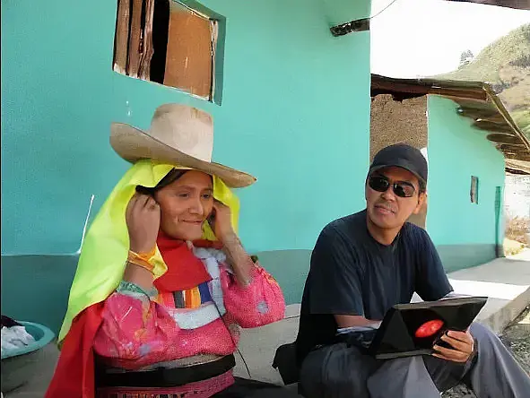 Ein Mann Anfang 40 mit Schildkappe und Sonnenbrille, der neben einer indigenen Frau sitzt.