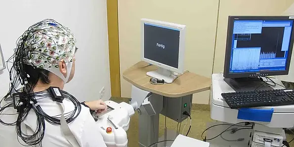 A person sits in front of a screen with electrodes on her head