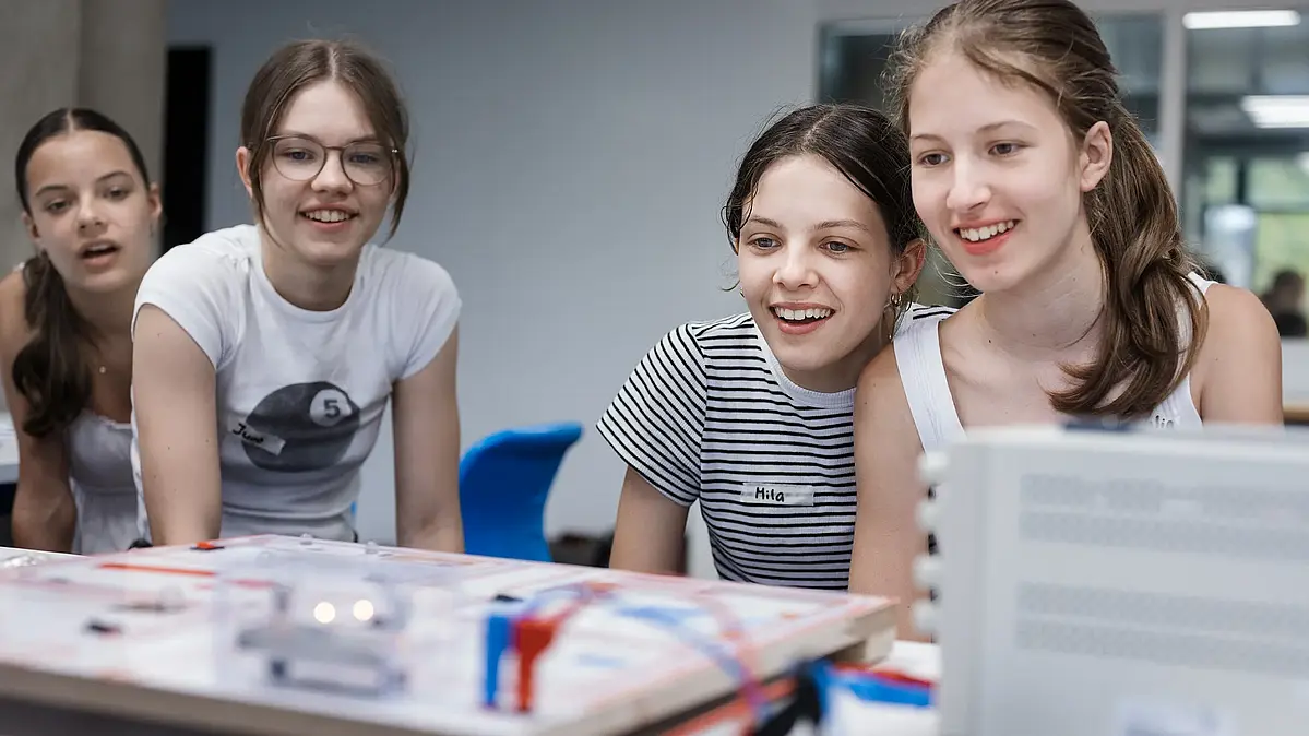 Vier junge Schülerinnen schauen lachend auf einen Schaltkreislauf. TüPhyLab