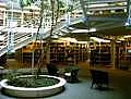 Mittig steht ein Baum, um den eine runde Treppe führt. Im Hintergrund sind Bücherregale der Bibliothek des Theologicums zu sehen.
