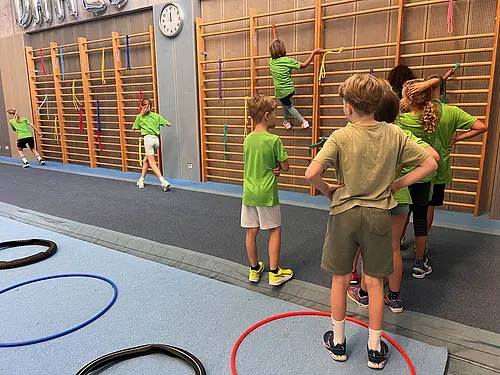 Kinder stehen vor einer Sprossenwand, ein Kind klettert. 