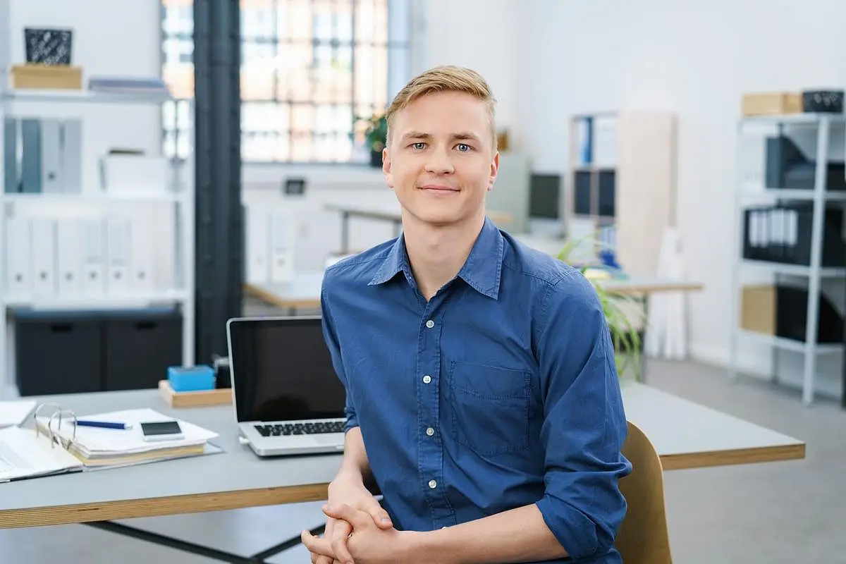 Junger Mann im Büro am Schreibtisch mit Laptop
