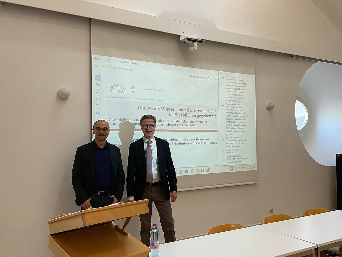 Auf dem Bild ist Herr Prof. Winter zusammen mit einem weiteren Mann zu sehen. Der Mann trägt kurz geschorene Haare, einen leichten Bart und eine runde, schwarze - sehr markante - Brille. Die Männer stehen vor einer Leinwand auf der Herr Winters erste Folie zum Vortrag sichtbar ist.