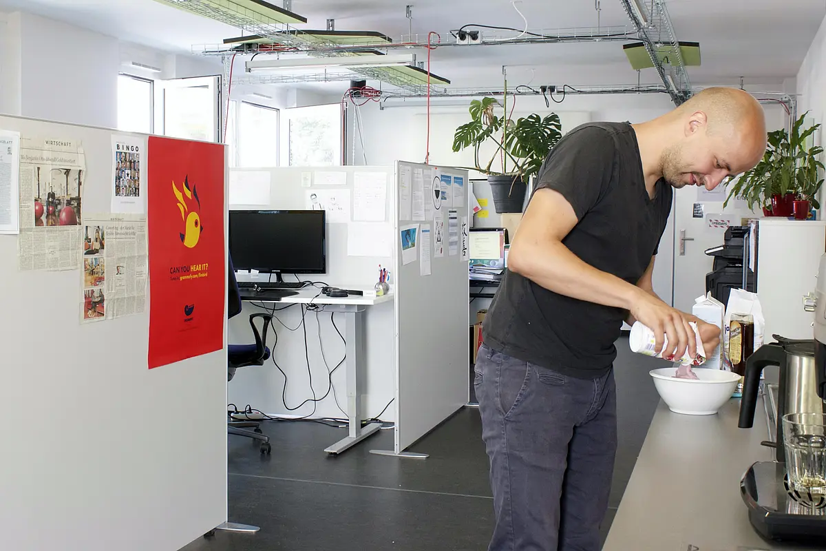 Elias genießt gewisse Freiheiten, die er sich in dem nicht ganz so konventionellen Büro nehmen kann. Er empfinde die denkstube ein Stück weit als zweites Zuhause, da sich einige seiner täglichen Gewohnheiten in den Coworking Space hinein verlagerten. Eine dieser Gewohnheiten lässt sich auf dieser Abbildung nachvollziehen: Ein morgendliches Frühstück, das er sich in der Gemeinschaftsküche zubereitet. Dass er dieses am Schreibtisch verzehren wird, stört keinen, genauso wenig, wenn er zwischendurch in den Supermarkt geht oder Privatgespräche am Telefon führt. 
