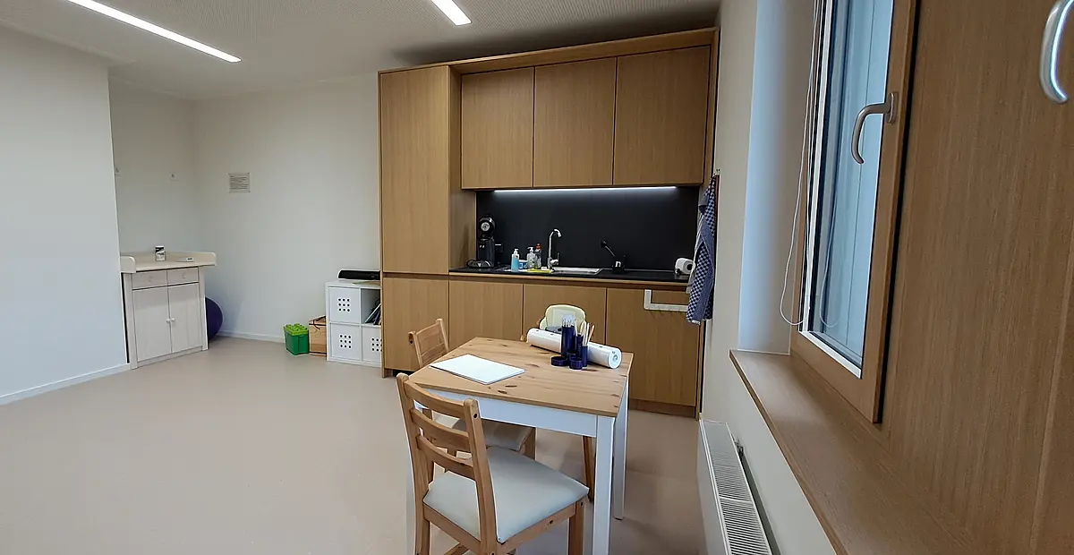 Tisch mit Stühlen und Küche im Familienzimmer Theologien/Campus Tal im ZITh-Neubau