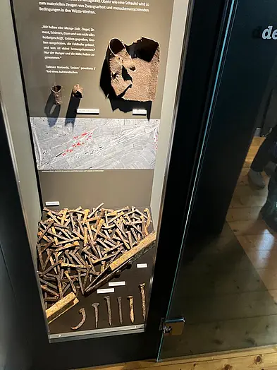 Spuren der Opfer? Vitrine mit archäologischen Funden, die Hinweise auf den Arbeitsalltag der Zwangsarbeiter geben, darunter Werkzeuge und Relikte des Feldbahnnetzes zum Transport von Ölschiefer. 