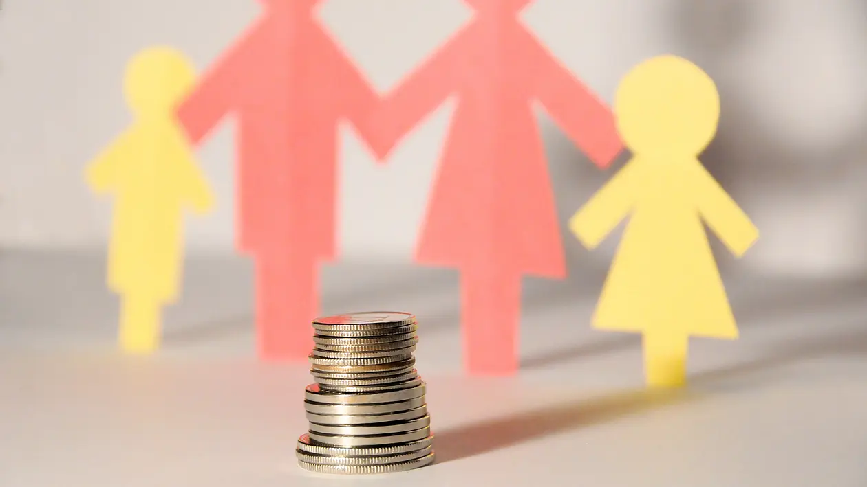 Kachelbild mit dem Scherenschnitt einer Familie mit zwei Kindern, Stapel Münzen im Vordergrund (Verlinkt zum Angebot KiBeKo – Finanzielle Unterstützung für Kinderbetreuung)