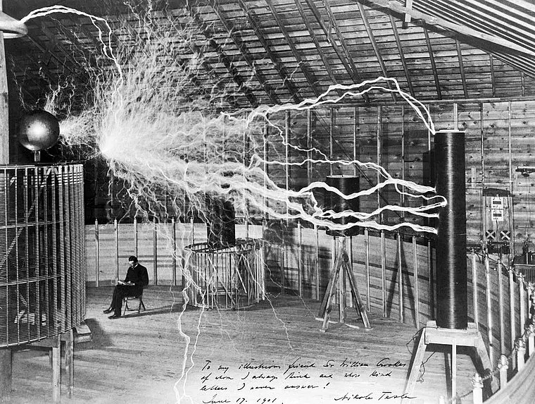 A man, probably Nikola Tesla, with his equipment for producing high-frequency alternating currents.
