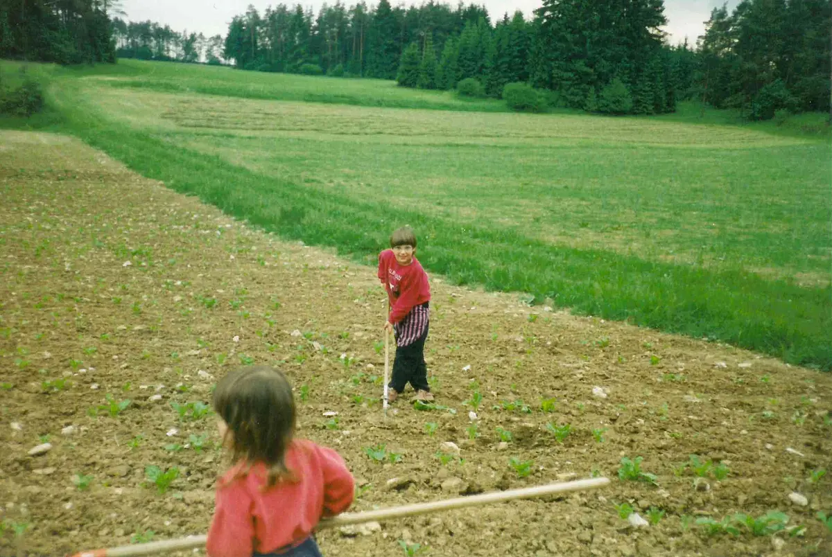 Kind mit Hacke auf einem Feld, ein zweites Kind im Vordergrund