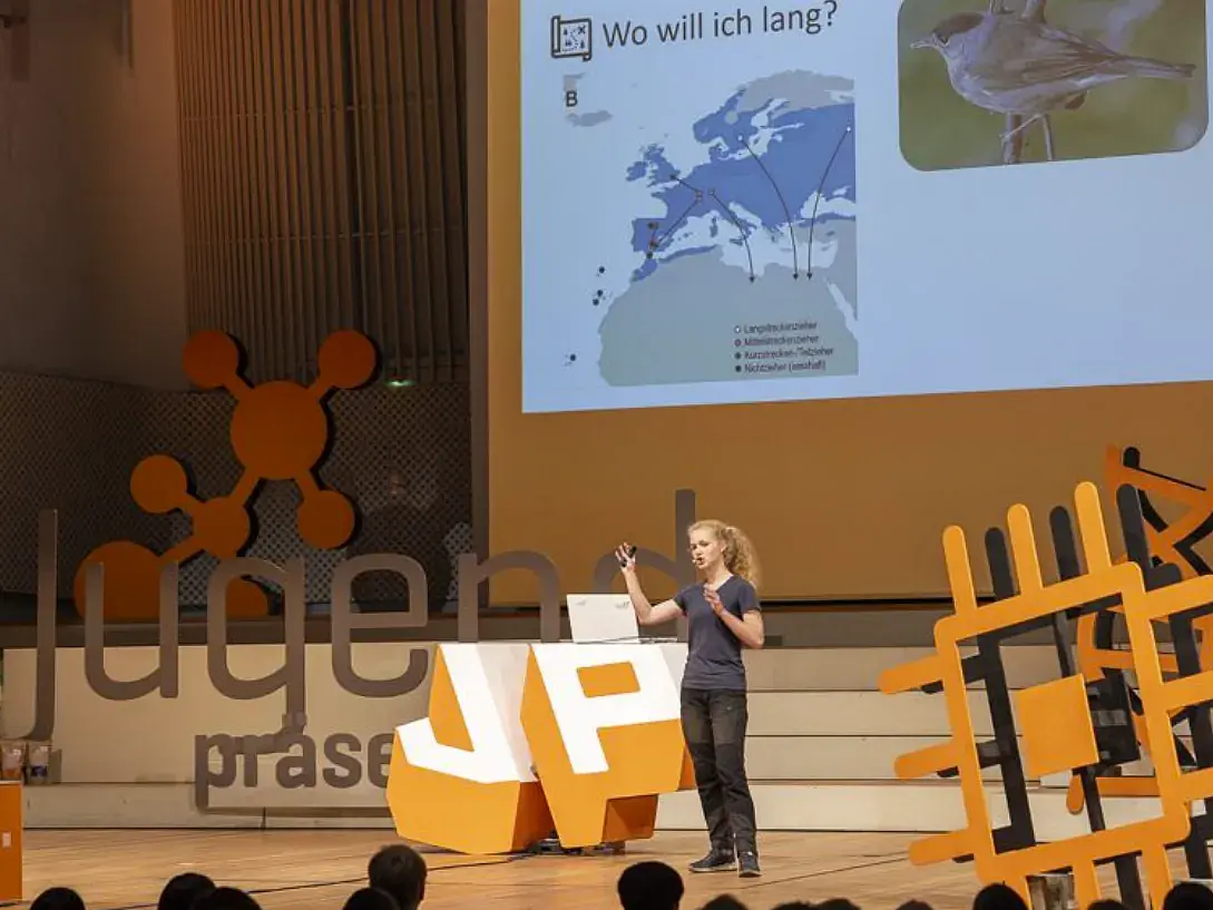 Eine junge Frau präsentiert etwas auf einer Bühne