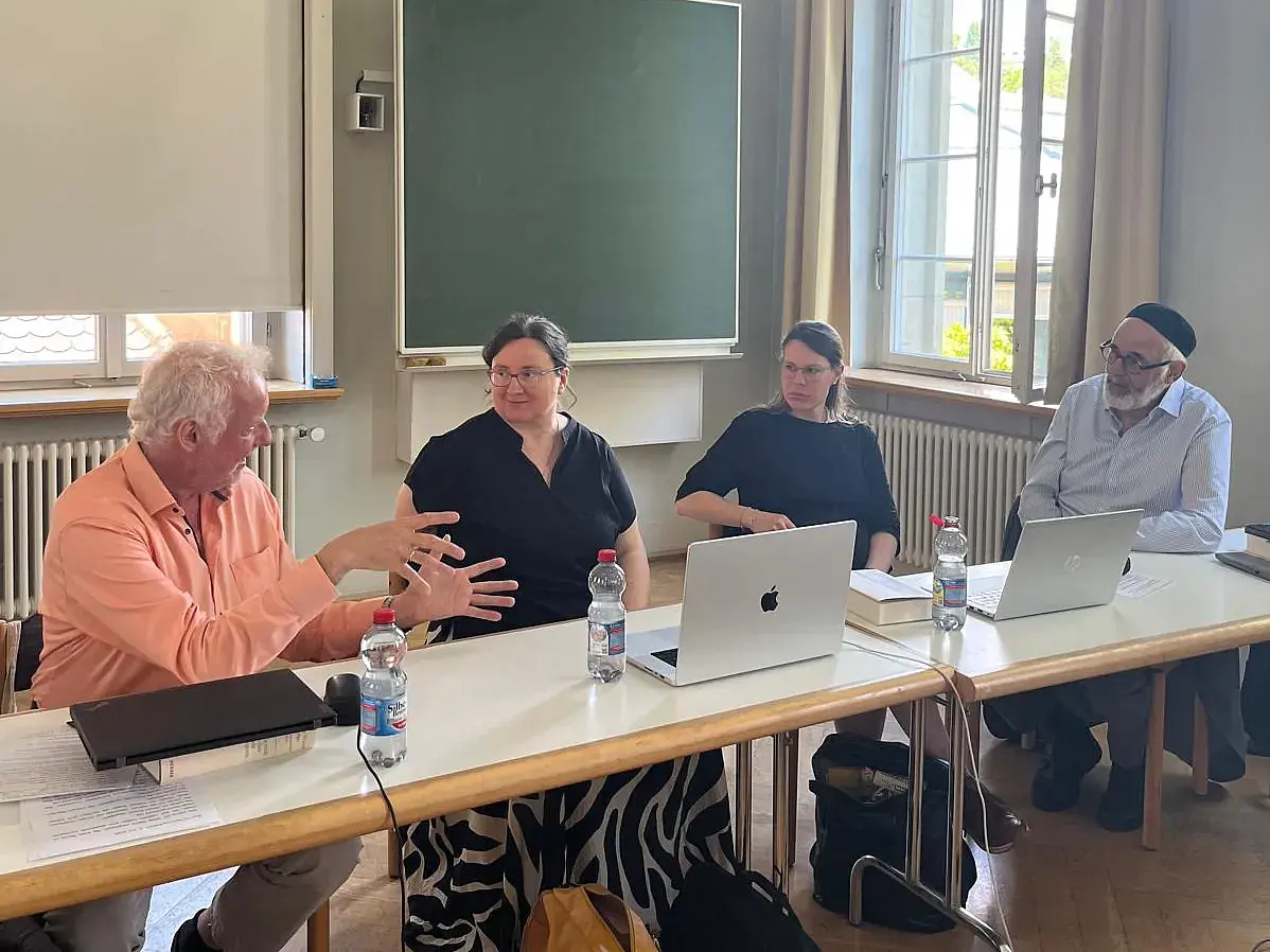 Vier Personen sitzen in einer Reihe an einem langen Tisch mit Laptops und sprechen zueinander. Die Personen sind von links nach rechts: Reinhold Boschki, Marion Eichelsdörfer, Elisabeth Migge und Daniel Krochmalnik