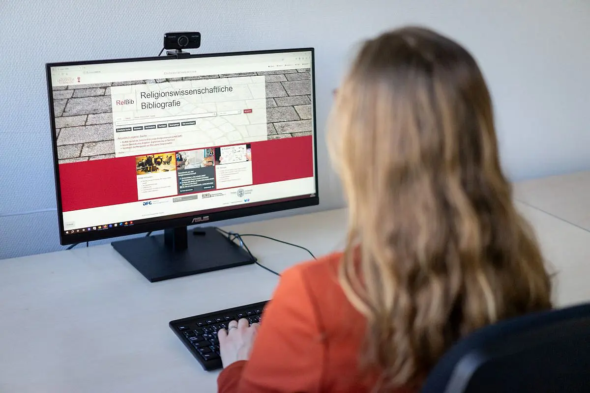 Die Religionswissenschaftliche Bibliografie (RelBib) ist eines von drei FID-Portalen, die an der UB Tübingen herausgegeben werden. Frau guckt auf Bildschirm mit neuem Portal.